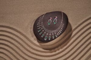 Diamond necklace and earrings set displayed on a brown stone with sand art background.
