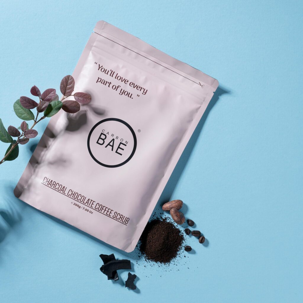 Carbon BAE charcoal coffee scrub pouch photographed on a blue background.
