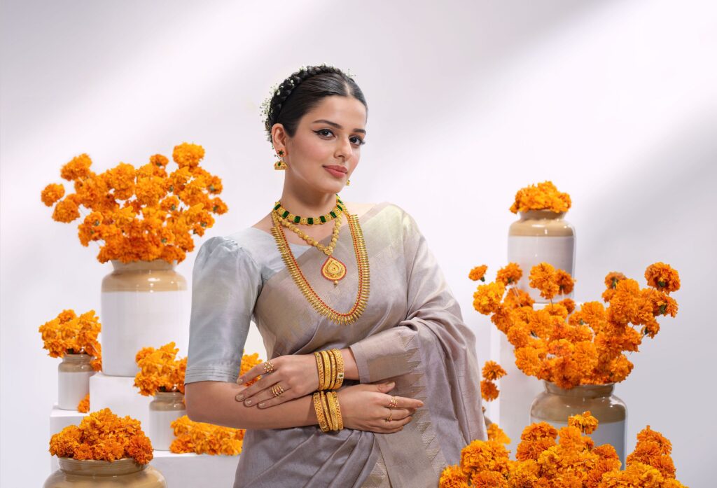 Woman in silver saree adorned with traditional gold jewelry, surrounded by vibrant orange marigold flowers.