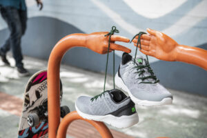 Gray PUCA sneakers with green laces hanging on orange hand-shaped stand.