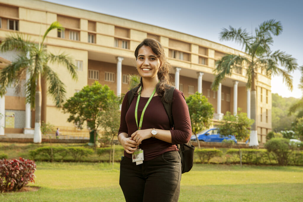 A student at GITAM University smiling outdoors on campus, with academic buildings and greenery in the background.