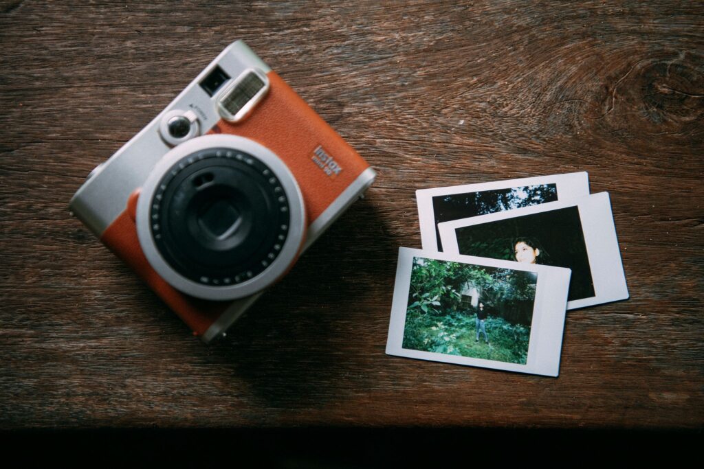 A vintage-style instant camera placed on a wooden surface beside three developed instant photos.