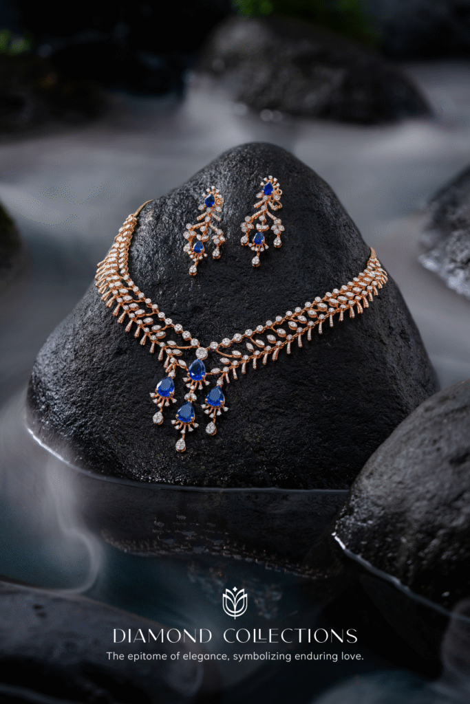 Tanmayi Diamond Collection: a diamond necklace and earrings with blue gemstones on a black rock against a misty background.