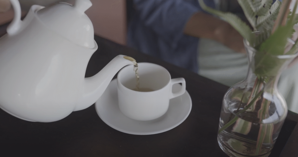 Tea being poured into a white cup beside a glass vase of green leaves at Paradisa Plantation Resort.