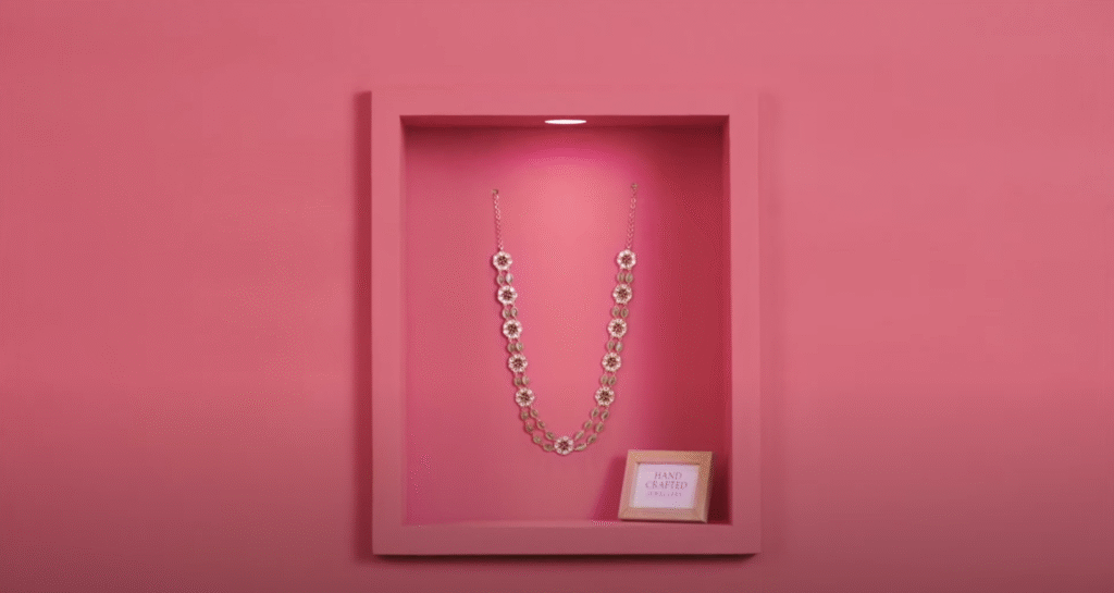 Elegant handcrafted necklace with floral design displayed in a pink showcase.