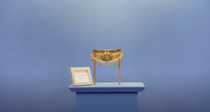Traditional gold waist belt with intricate floral design and hanging embellishments on display stand.