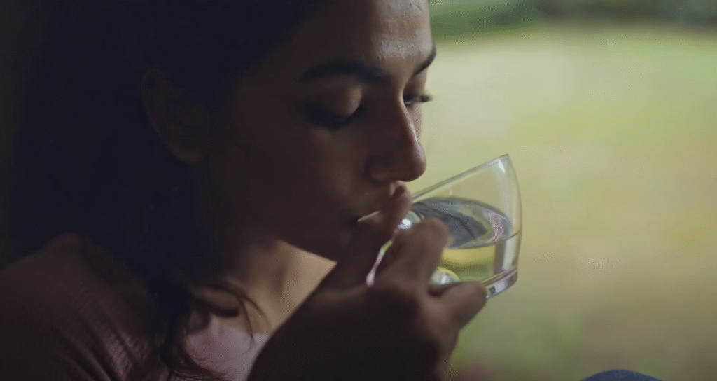 Close-up of a woman drinking water from a glass near a window with natural light.