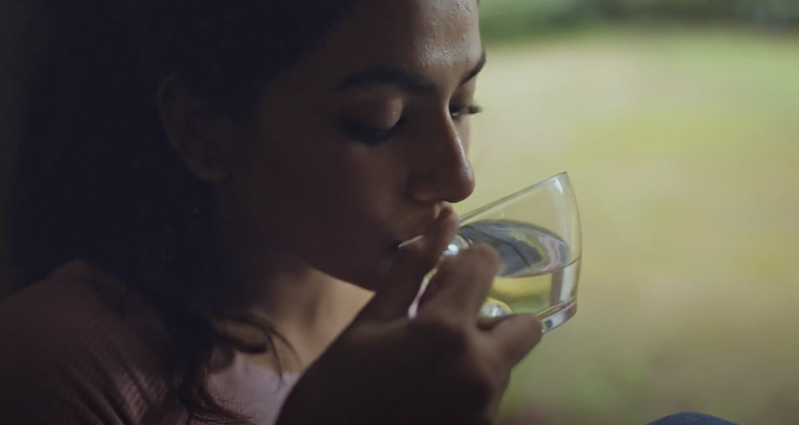 Close-up of a woman drinking water from a glass near a window with natural light.