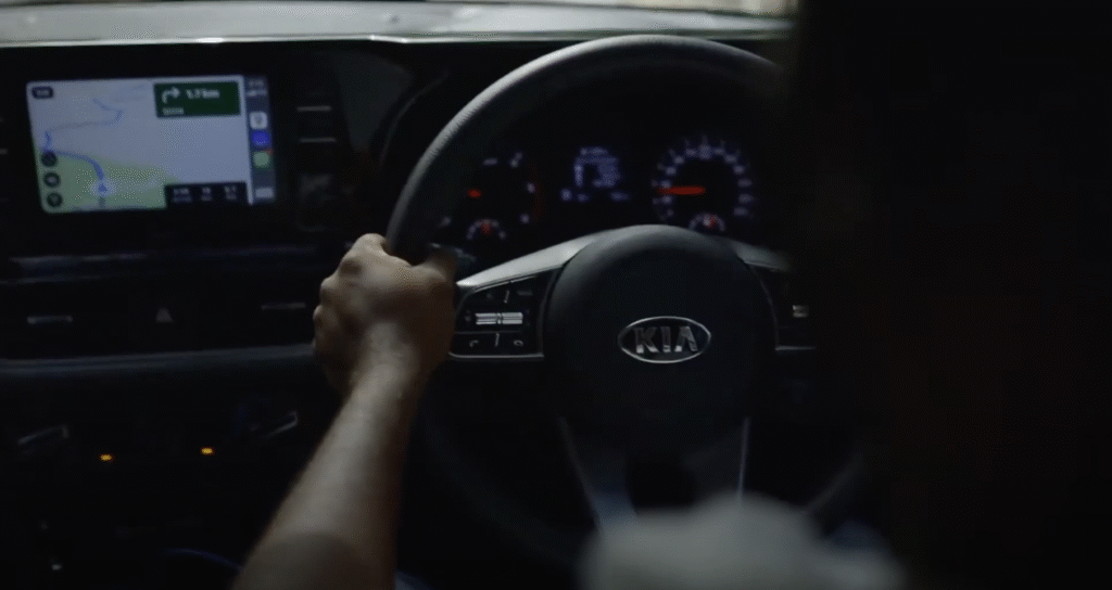 Close-up of a driver’s hands on a Kia steering wheel with GPS navigation on the car’s dashboard screen.