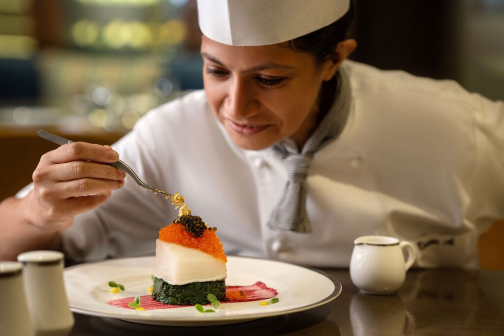 Chef carefully plating a gourmet dish topped with caviar and garnishes.