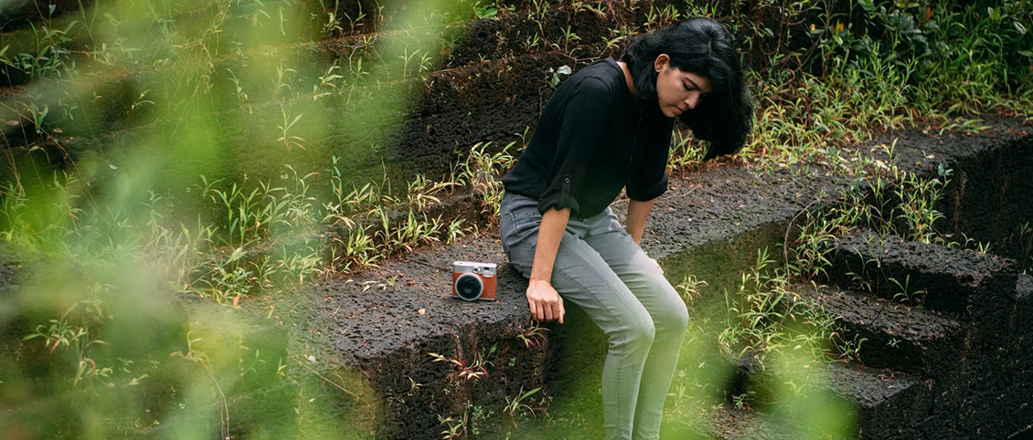 Woman sitting on stone steps in a lush outdoor setting with a camera placed beside her.