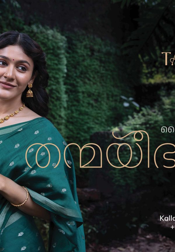 A woman in a green saree adorned with gold jewelry, smiling gracefully against a lush green backdrop, showcasing Thanmayi Jewellery.